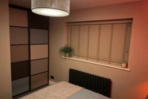 Bedroom with warm lighting, featuring a bed, a modern sliding wardrobe with woodwork panels.