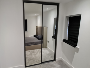 A bedroom with a bed, a mirror, and a sleek two-door black sliding wardrobe.