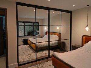 A stylish bedroom featuring a cozy bed, and a sleek four-door black sliding wardrobe.