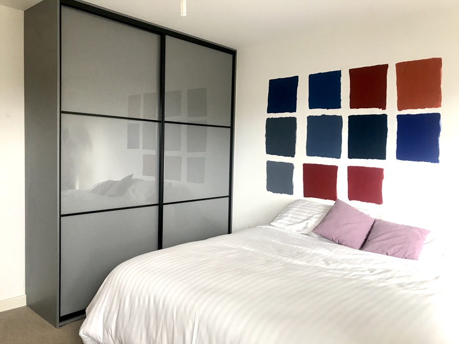 A bedroom featuring a bed, a wall adorned with colorful pictures, and a two-door glass sliding wardrobe.