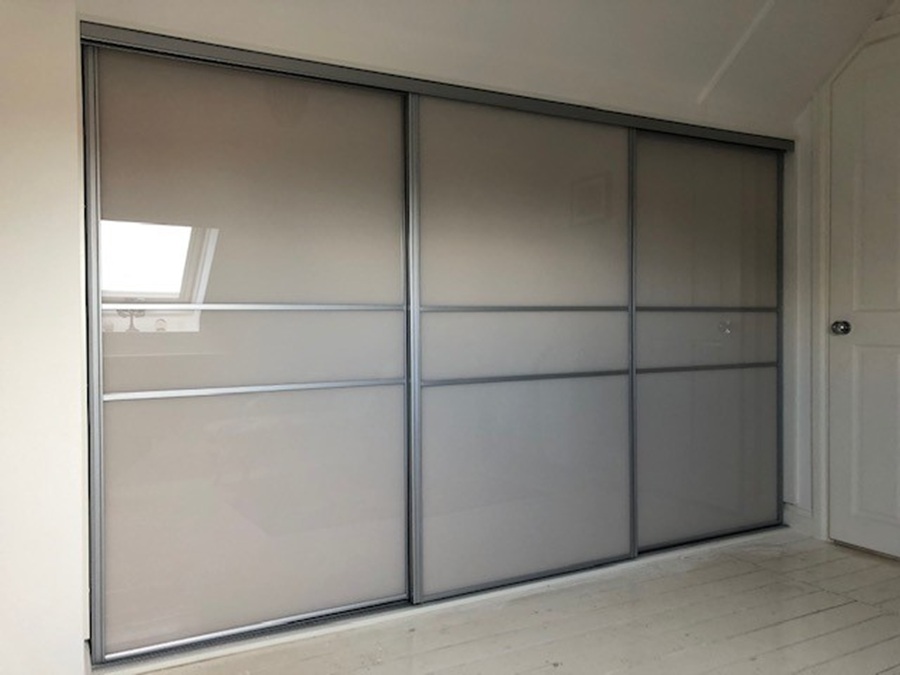A room showcasing a three-door glass sliding wardrobe with elegant glass panels