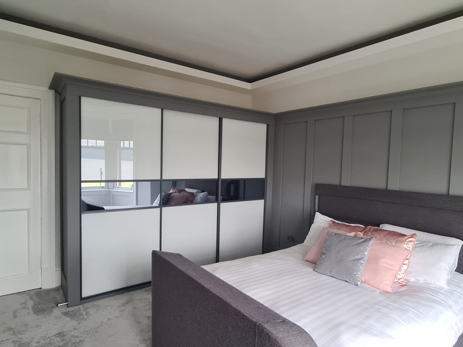 A 3 Door Glass Sliding Wardrobe with white glass & mirror doors in an beautifully decorated room