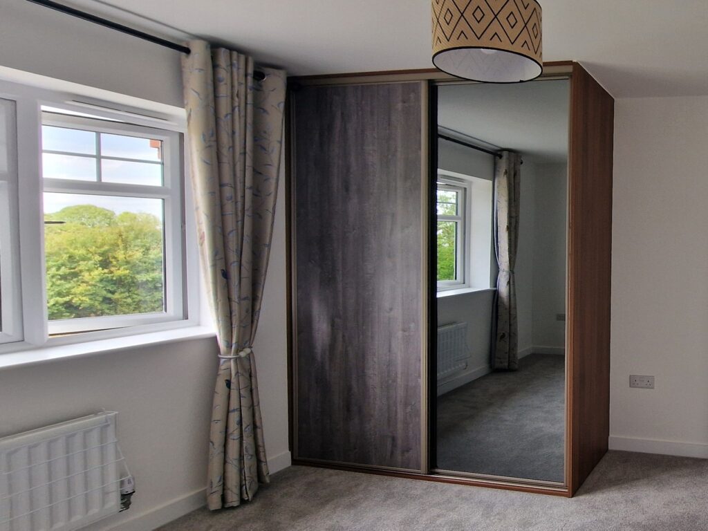 A bedroom featuring a two-door mirror sliding wardrobe reflecting the room's decor.