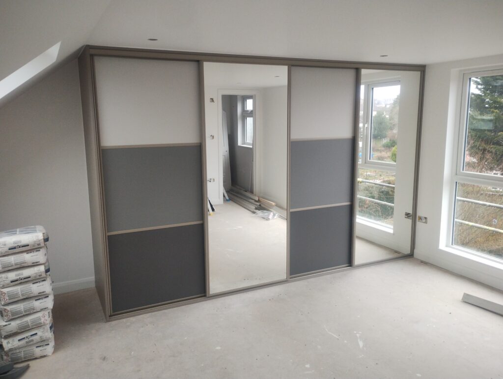 Spacious room with beige walls features a modern sliding wardrobe with mirrored panels. Large windows overlook a garden, creating a bright and airy feel.