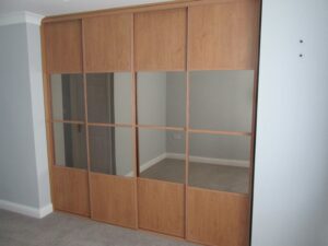 Woodwork wardrobe with sliding oak mirrored doors in a light gray room.