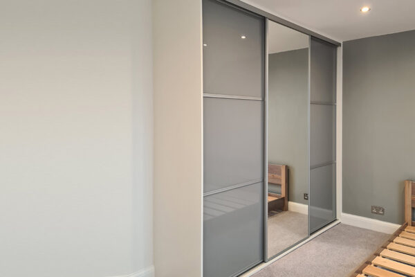 Triple panel glass sliding wardrobe with central mirror door.