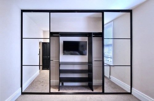 Fitted sliding wardrobe with concealed TV unit for the perfect wardrobe interior idea.