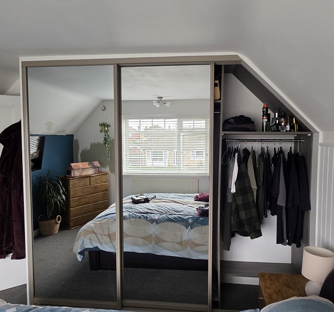 Open sliding wardrobe underneath a sloped ceiling showing organised hanging space and storage